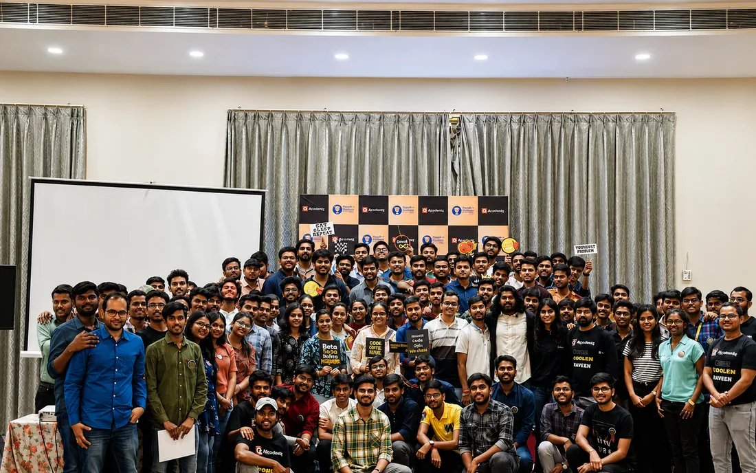 About a hundred students standing and seated together for a group photograph at a campus event, several holding hand-lettered placards