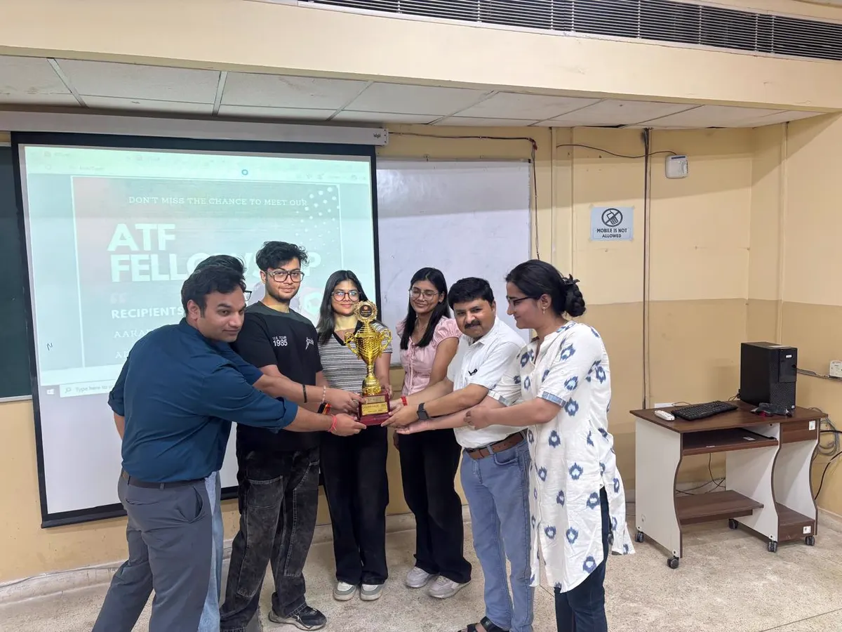 A group of ATF fellows and faculty holding the cohort trophy together in front of an ATF fellowship slide at IIIT Gwalior