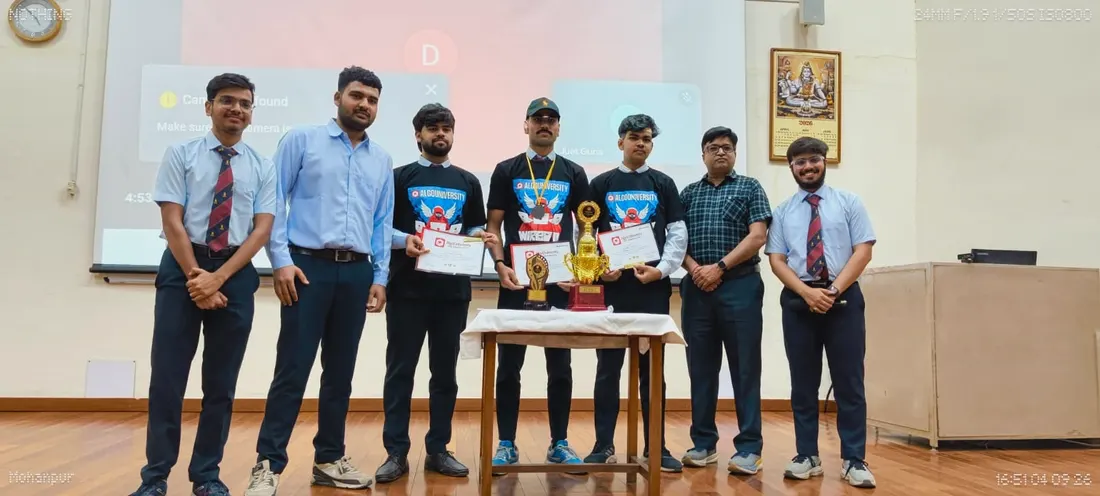 Students in formal uniform standing with faculty behind a table holding two trophies and certificates