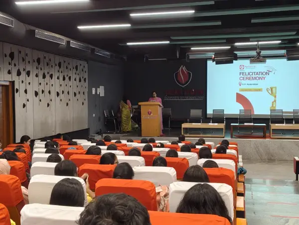 A full auditorium of seated students facing a felicitation ceremony slide