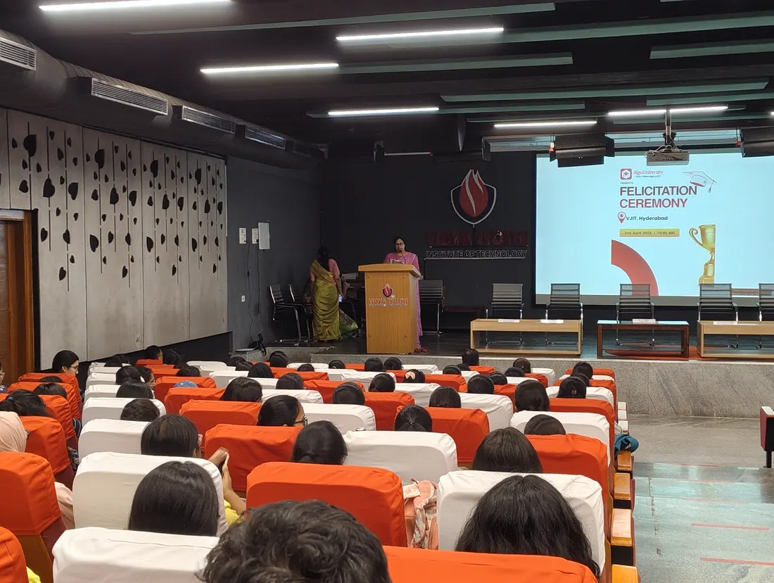A full auditorium of seated students facing a felicitation ceremony slide