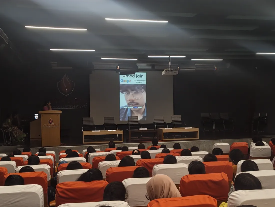 A darkened auditorium with a slide on screen showing a fellow's photograph and the stipend of his offer