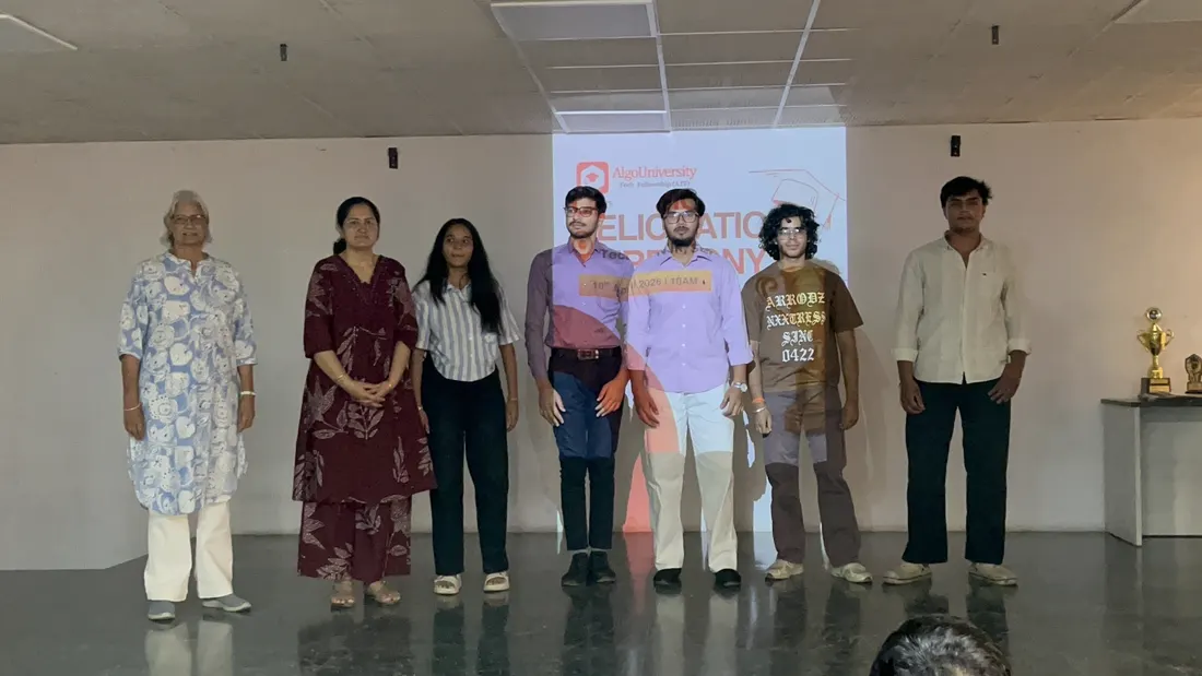 Six students standing on stage with a trophy in front of a felicitation ceremony slide