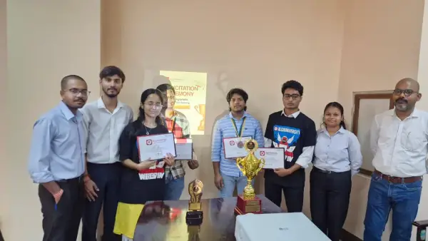 A group of students and faculty standing with two trophies in front of a felicitation ceremony slide