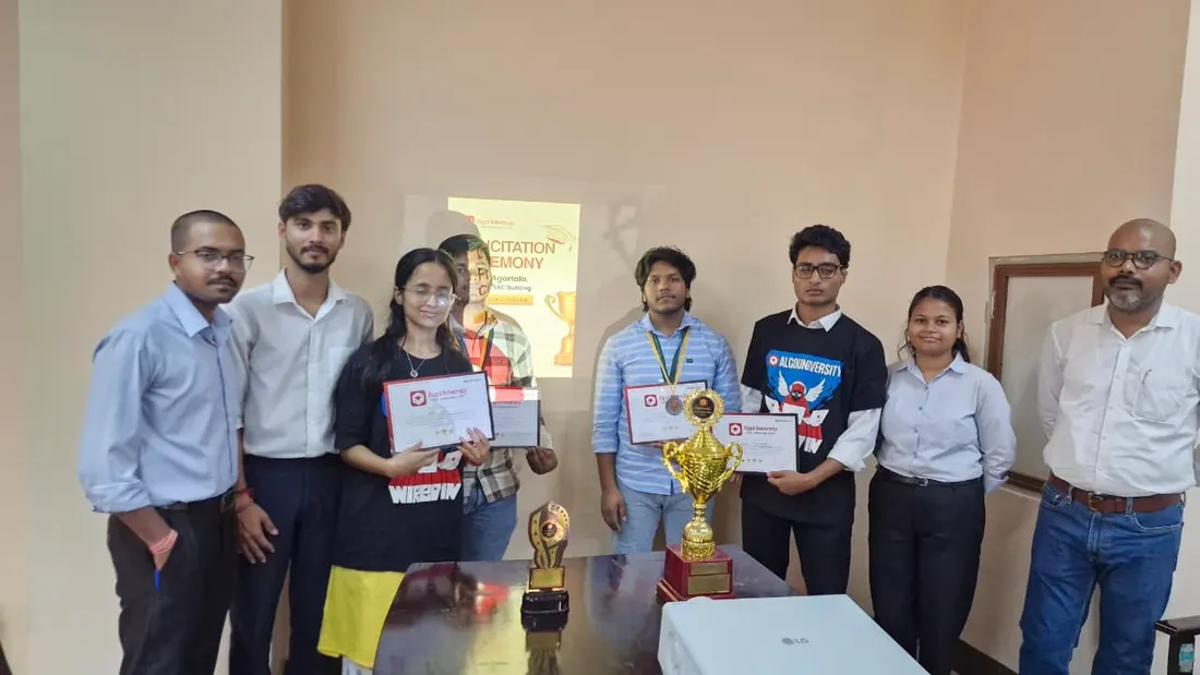A group of students and faculty standing with two trophies in front of a felicitation ceremony slide